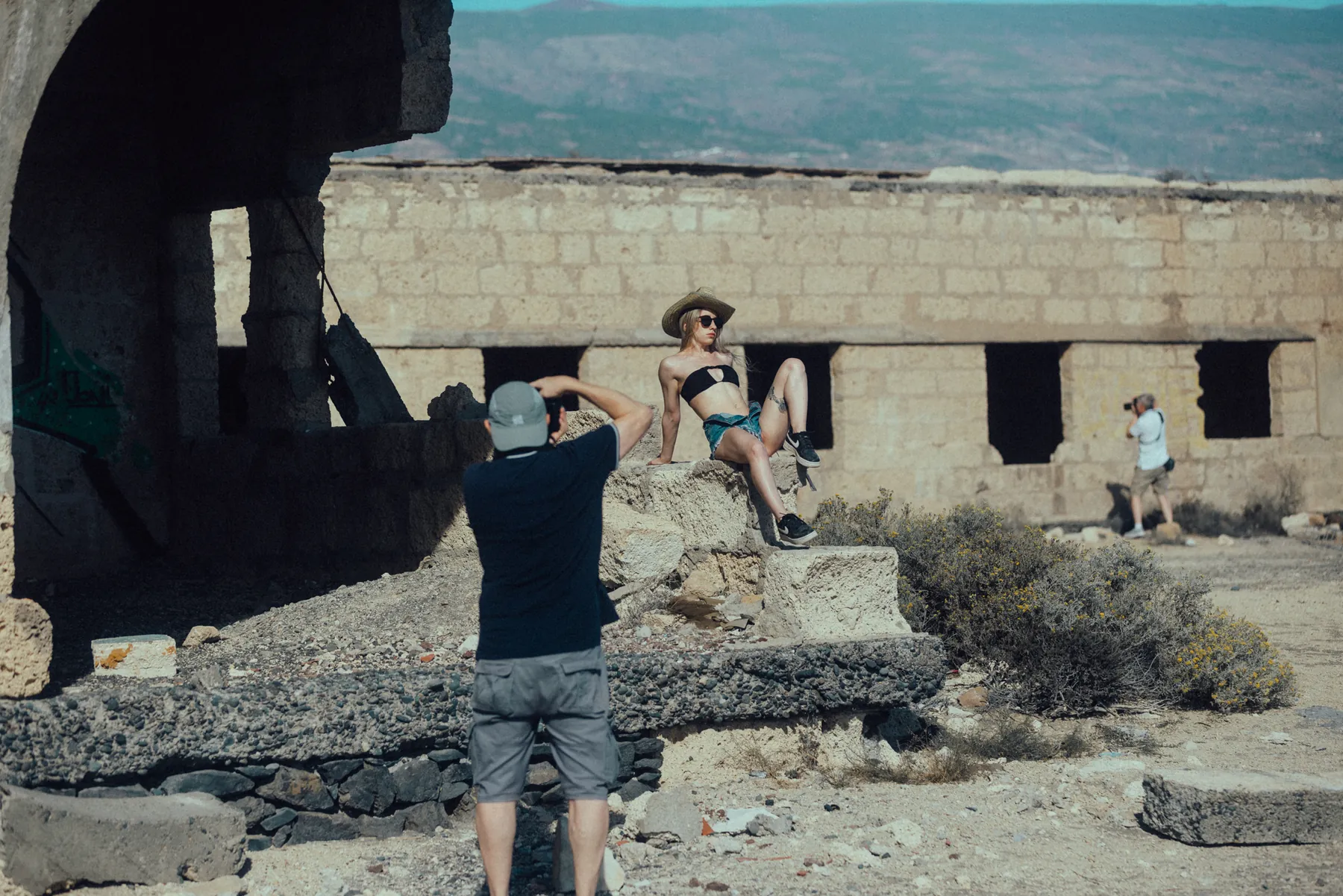 Making-of: Ein Fotograf fotografiert ein Model im Bikini an einer alten Steinruine, hinten ein zweiter Fotograf