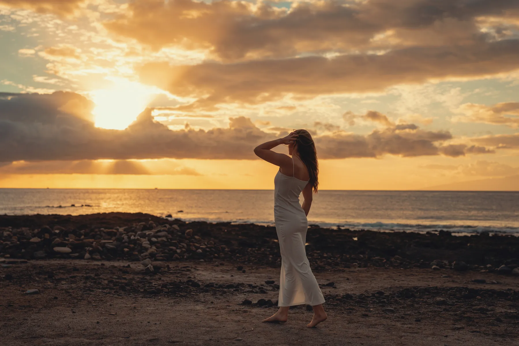 Model im weißen Kleid von hinten an der Küste im Sonnenuntergang