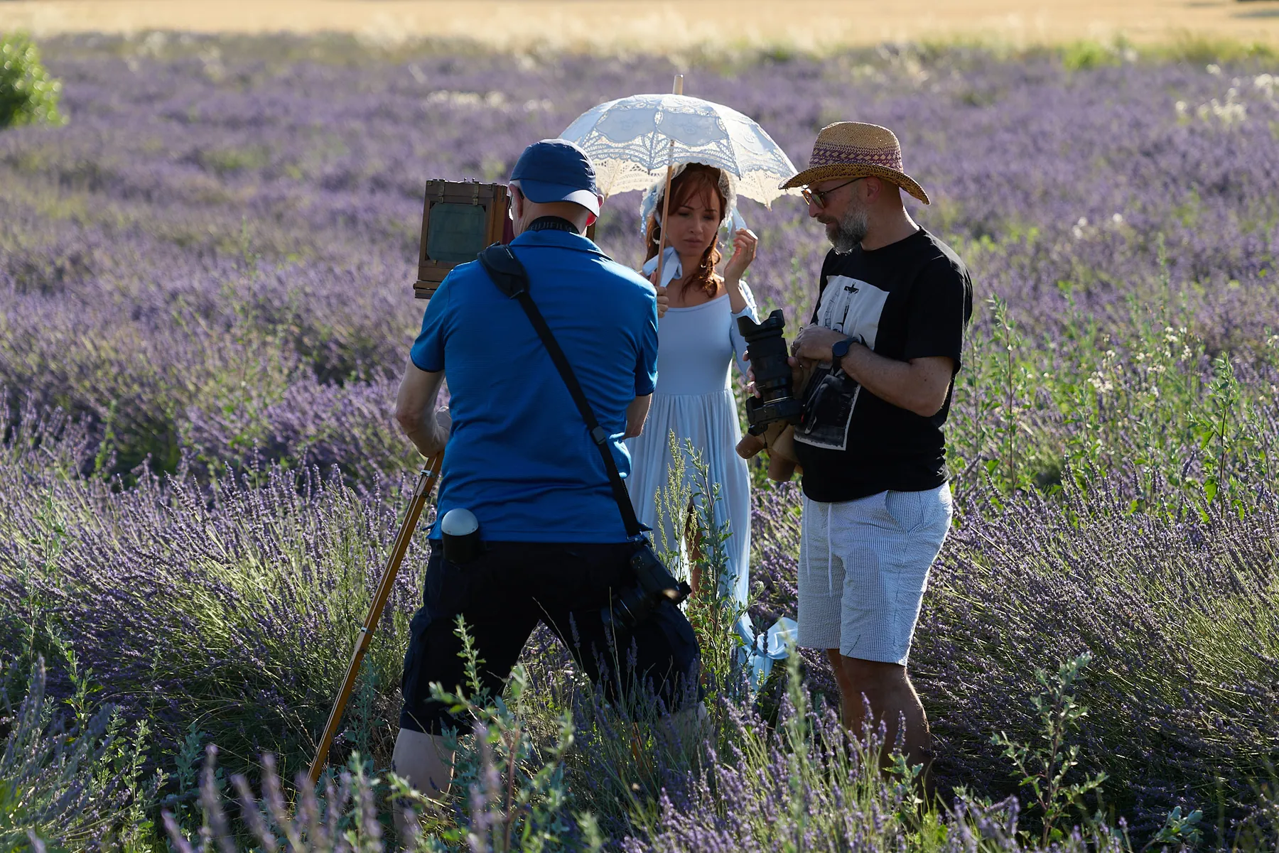 Making-of im Lavendelfeld: Fotografen fotografieren ein Model im weißen Kleid mit Sonnenschirm