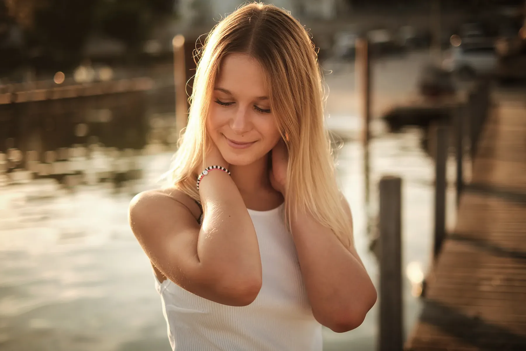 Blonde woman in a white top by the water against the light