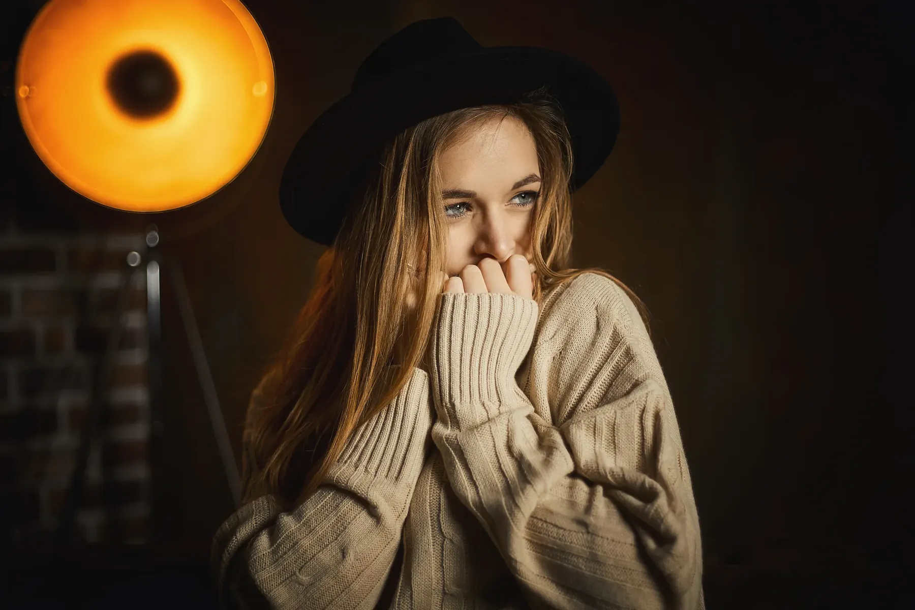 Frau mit Hut und Strickpullover vor einer Leuchte